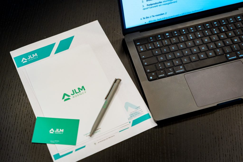 Foto van een bureau met laptop en JLM Agency-logo, benadrukt webdesign en websiteontwikkeling.